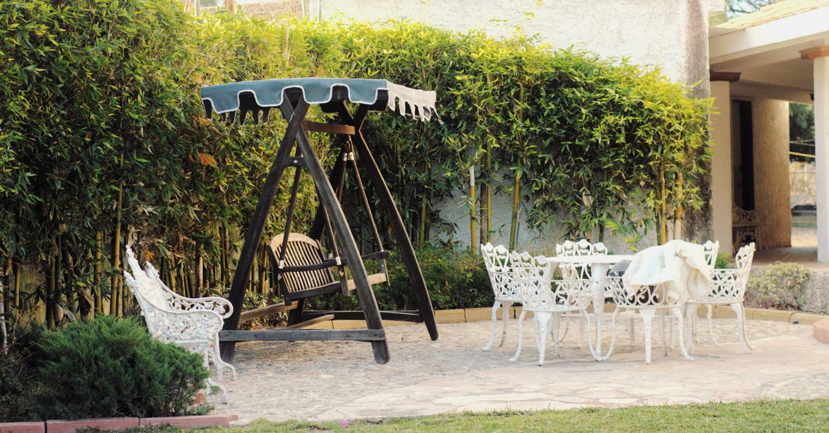 Cozy outdoor patio with vintage furniture and swing, surrounded by lush greenery.